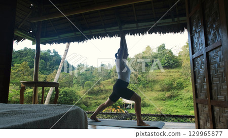 Yoga practice on bamboo terrace with view of rice fields and lush plants as woman enjoys morning calm  129965877