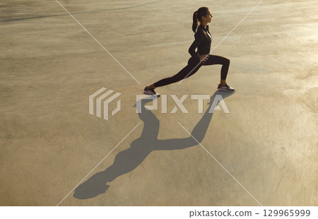 Sporty young girl doing stretching exercise at outdoor morning workout on city street 129965999