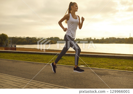 Young slim sporty woman wearing sportswear running in the park along the river. Young slim sporty woman wearing sportswear running in the park along the river. 129966001
