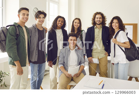 Male teacher standing with high school students and looking at camera in the classroom. 129966003