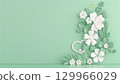 On a green background, an application of flowers, leaves, and a white outline of a heart. Copy space 129966029