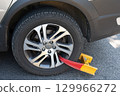 Yellow and red wheel clamp on car tire. 129966272