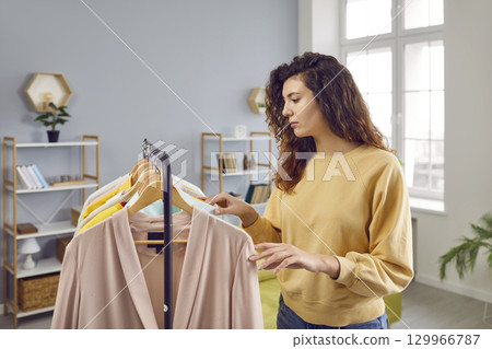 Young woman looking at different outfits on clothes rack and choosing what to wear Young woman looking at different outfits on clothes rack and choosing what to wear 129966787