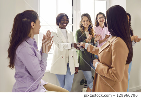 Two businesswomen shaking hands while colleagues applauding them in office Two businesswomen shaking hands while colleagues applauding them in office 129966796