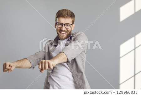 Happy, cheerful young man in a casual shirt and glasses is dancing and having fun Happy, cheerful young man in a casual shirt and glasses is dancing and having fun 129966833