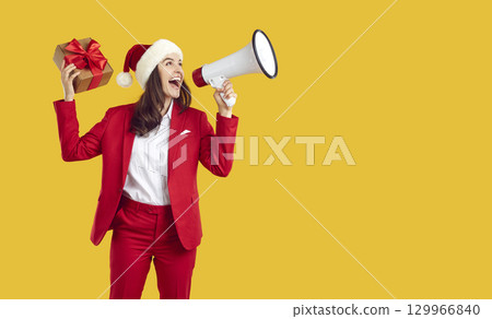 Brunette woman wearing red suit is talking in loudspeaker with giftbox on yellow background. 129966840