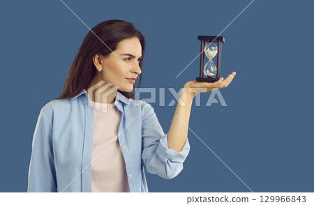 Young woman thinking while looking at sand glass that she is holding in her hand 129966843