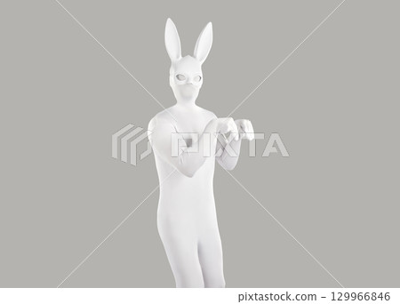 Funny man in a white bodysuit and rabbit mask jumping like a rabbit on a gray studio background Funny man in a white bodysuit and rabbit mask jumping like a rabbit on a gray studio background 129966846