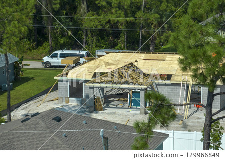 Aerial view of builders working on unfinished residential house with wooden roof frame structure under construction in Florida suburban area 129966849