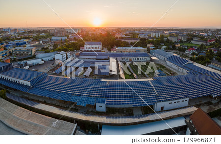 Aerial view of solar power plant with blue photovoltaic panels mounted on industrial building roof for producing green ecological electricity at sunset. Production of sustainable energy concept 129966871