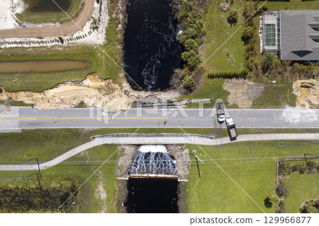 Construction trucks blocking road access at destroyed bridge after hurricane flooding in Florida. Equipment at roadwork site. Reconstruction of damaged road after flood water washed away asphalt 129966877