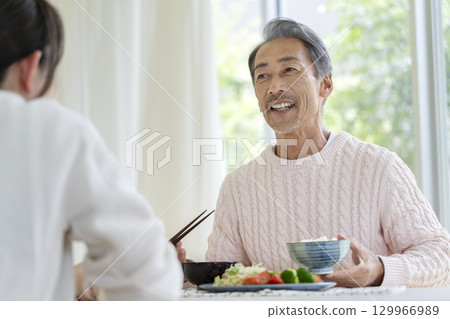 A smiling man in his 60s eating a meal 129966989