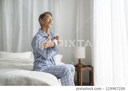 穿著睡衣的老人坐在床上伸展身體 129967289