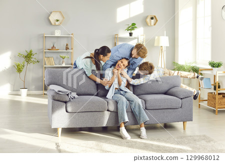 Happy laughing teenage child girl having fun tickling with parents and brother sitting at home Happy laughing teenage child girl having fun tickling with parents and brother sitting at home 129968012