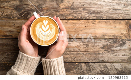 Woman's hand holding latte art coffee on a wooden table 129968313
