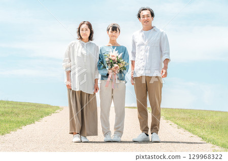 藍天下的三位父母和孩子（花束，禮物，生日，家庭旅行，家庭，父親，母親，女兒） 129968322