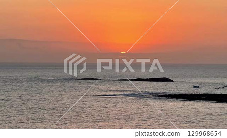 A Serene Sunset Over the Ocean with Silhouetted Rocks that Creates a Stunning Visual Scene 129968654