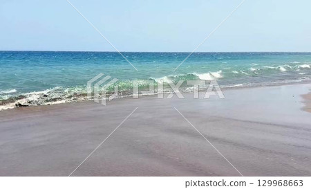 Serene Beach Waves Gently Lapping Against the Tranquil Shoreline Under Clear Blue Skies 129968663