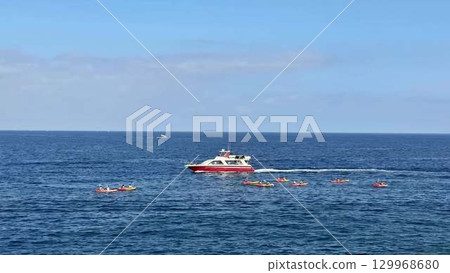 Adventurous individuals are kayaking near a motorboat amidst the beautiful, clear, and blue waters 129968680