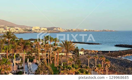 Enjoy a stunning sunset view with palm trees and a rocky shoreline along the coast 129968685
