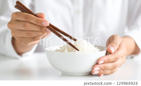 Close-up of a woman's hands eating white rice with chopsticks 129968928