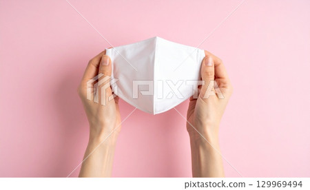 Woman's hand holding a white cloth mask and pink background Woman's hand holding a white cloth mask and pink background 129969494