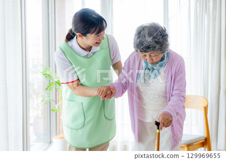 Care image: Senior woman walking with a cane and a caregiver 129969655