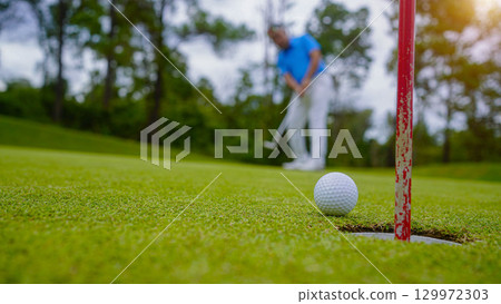 Golfer putting ball on the green golf, lens flare on sun set evening time. Golfer hitting golf ball. Golfer putting ball on the green golf, lens flare on sun set evening time. Golfer hitting golf ball. 129972303