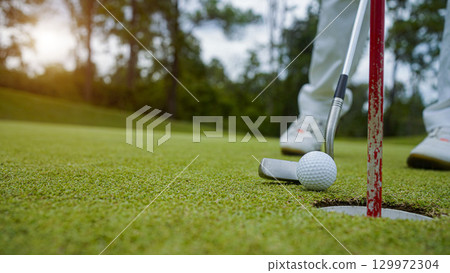 Golfer putting ball on the green golf, lens flare on sun set evening time. Golfer hitting golf ball. Golfer putting ball on the green golf, lens flare on sun set evening time. Golfer hitting golf ball. 129972304