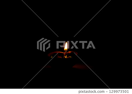 Burning Clay Oil Lamp in Darkness Symbolizing Light and Hope 129973501