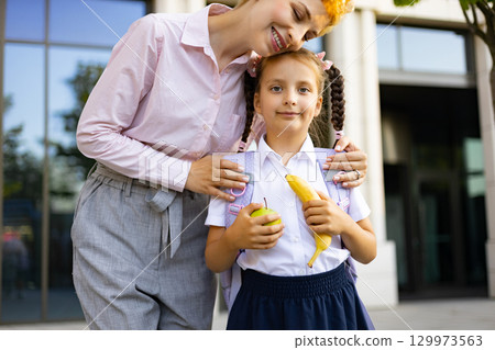 A mother lovingly embraces her daughter in a schoolyard, preparing for the school day. A mother lovingly embraces her daughter in a schoolyard, preparing for the school day. 129973563
