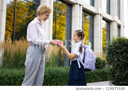 A mother hands her daughter a lunchbox outside a school building, symbolizing back-to-school moments. A mother hands her daughter a lunchbox outside a school building, symbolizing back-to-school moments. 129973589