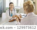 Orthopedist offering orthopedic insoles to patient at appointment, holding two orthotic insets 129973612