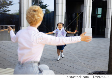 A mother and daughter embrace outside a school building, capturing a moment of joy and affection. 129973698