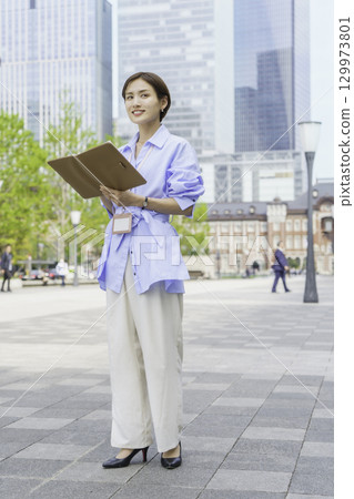 Portrait of a young businesswoman standing with a notebook in an office district, vertical position 129973801