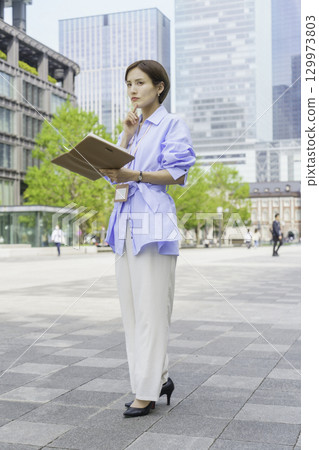 Portrait of a young businesswoman standing with a notebook in an office district, vertical position Portrait of a young businesswoman standing with a notebook in an office district, vertical position 129973803