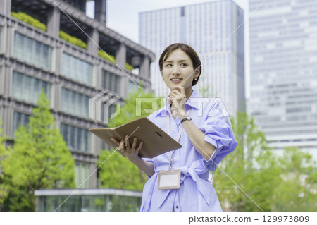 一位年輕女商人站在辦公區拿著筆記本的畫像 129973809