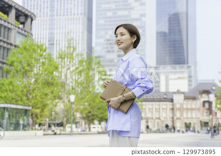 一位年輕女商人站在辦公區拿著筆記本的畫像 129973895
