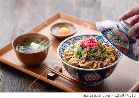 日式餐桌上擺放著熱騰騰的牛肉套餐和加了醃菜的味噌湯。這是一張傳統日式午餐或晚餐的圖片。 日式餐桌上擺放著熱騰騰的牛肉套餐和加了醃菜的味噌湯。這是一張傳統日式午餐或晚餐的圖片。 129974118