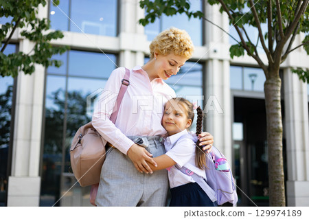 A mother embracing her student daughter outside a school building, symbolizing care and support. A mother embracing her student daughter outside a school building, symbolizing care and support. 129974189