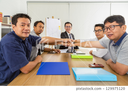 Group of business people joining, holding hands showing teamwork in the office. Group of business people joining, holding hands showing teamwork in the office. 129975120