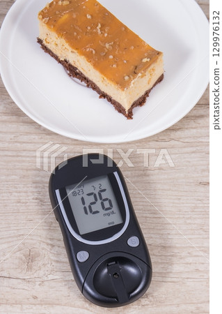 Glucometer and portion of cheesecake. Measuring and checking sugar level during diabetes Glucometer and portion of cheesecake. Measuring and checking sugar level during diabetes 129976132