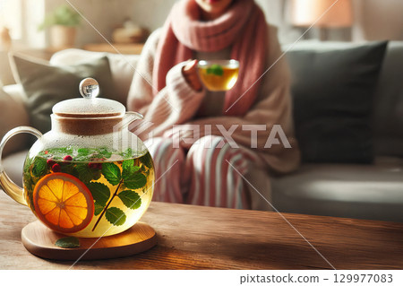 Glass teapot with herbal tea and fruits on a wooden table, cozy living room background, warm and relaxing atmosphere concept, winter season, flu season 129977083