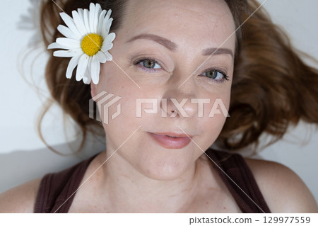 Woman With a Flower in Her Hair Relaxing Indoors Surrounded by Soft Light Woman With a Flower in Her Hair Relaxing Indoors Surrounded by Soft Light 129977559