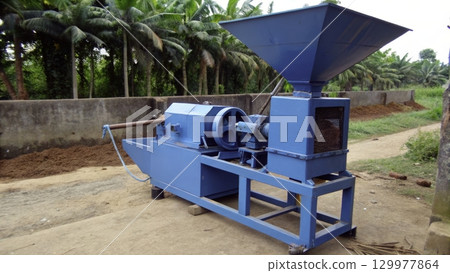Blue agricultural machine for processing located in a rural area surrounded by palm trees 129977864