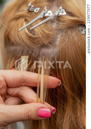 Hair Extension Application Process Close Up. A hairdresser holds a strand of hair in his hand 129977977