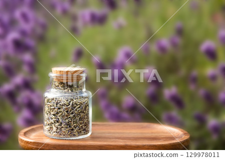 Glass Jar Filled with Dried Lavender on Wooden Tray with Lavender Background Outdoors Glass Jar Filled with Dried Lavender on Wooden Tray with Lavender Background Outdoors 129978011