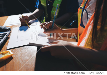 Closeup of team of industrial engineers meeting analyze machinery blueprints consult project on table in manufacturing factory. Working in manufacturing plant or production plant. 129978228