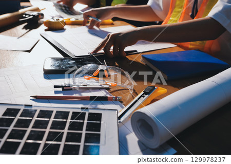 Closeup of team of industrial engineers meeting analyze machinery blueprints consult project on table in manufacturing factory. Working in manufacturing plant or production plant. 129978237