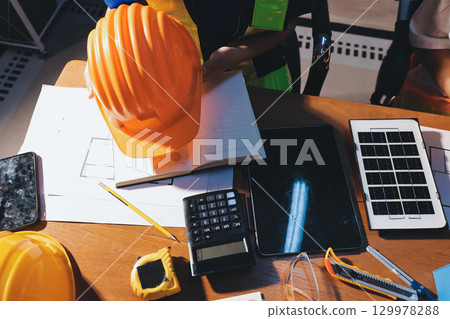 Closeup of team of industrial engineers meeting analyze machinery blueprints consult project on table in manufacturing factory. Working in manufacturing plant or production plant. 129978288